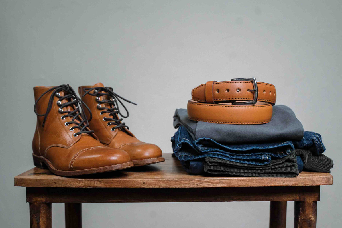 Italian Casual Belt in English Tan, coiled on folded jeans beside tan leather boots