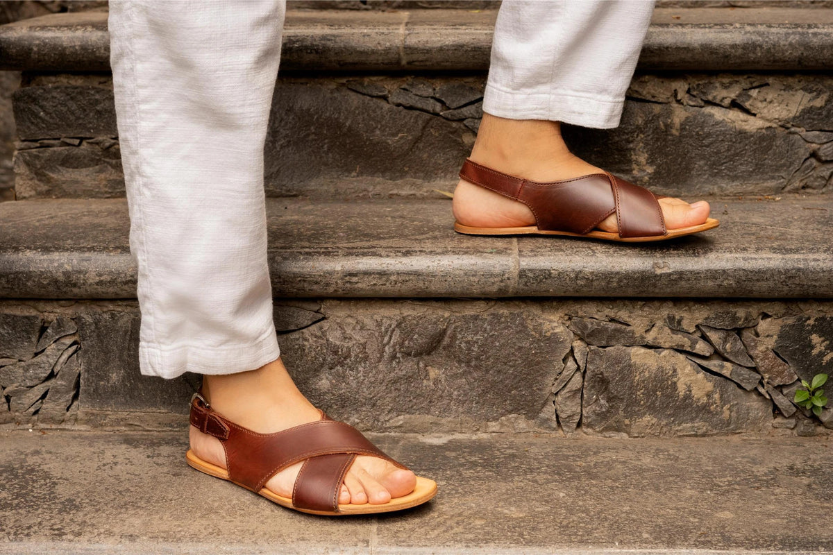 Jesus Sandals in Chestnut on foot, a person in white linen pants climbing old stone stairs