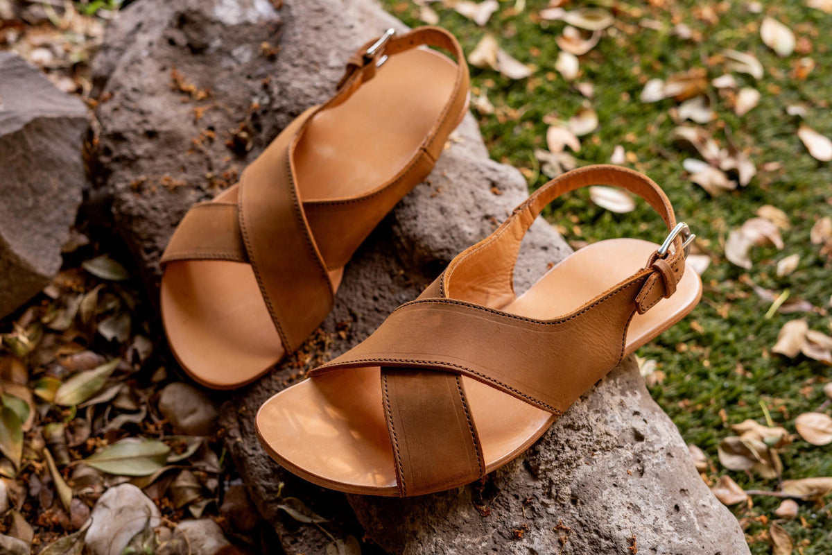 Jesus Sandals in Tobacco, a pair with crisscross straps and buckled heel straps on a mossy rock with fallen leaves