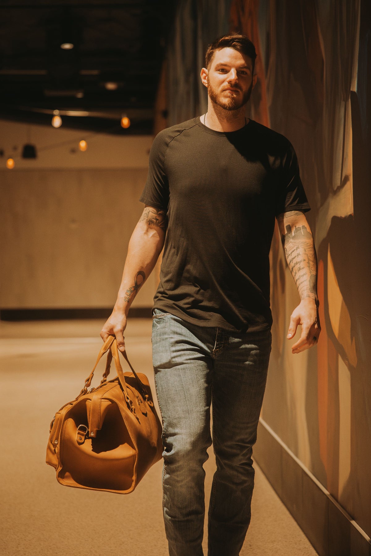 Jonah Heim walking down a corridor carrying a tan leather duffle bag.