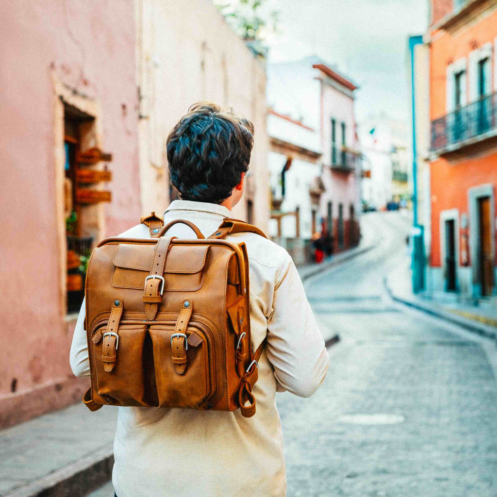 Big Mouth Leather Backpack in Tobacco, worn by a man walking down a colorful cobblestone street