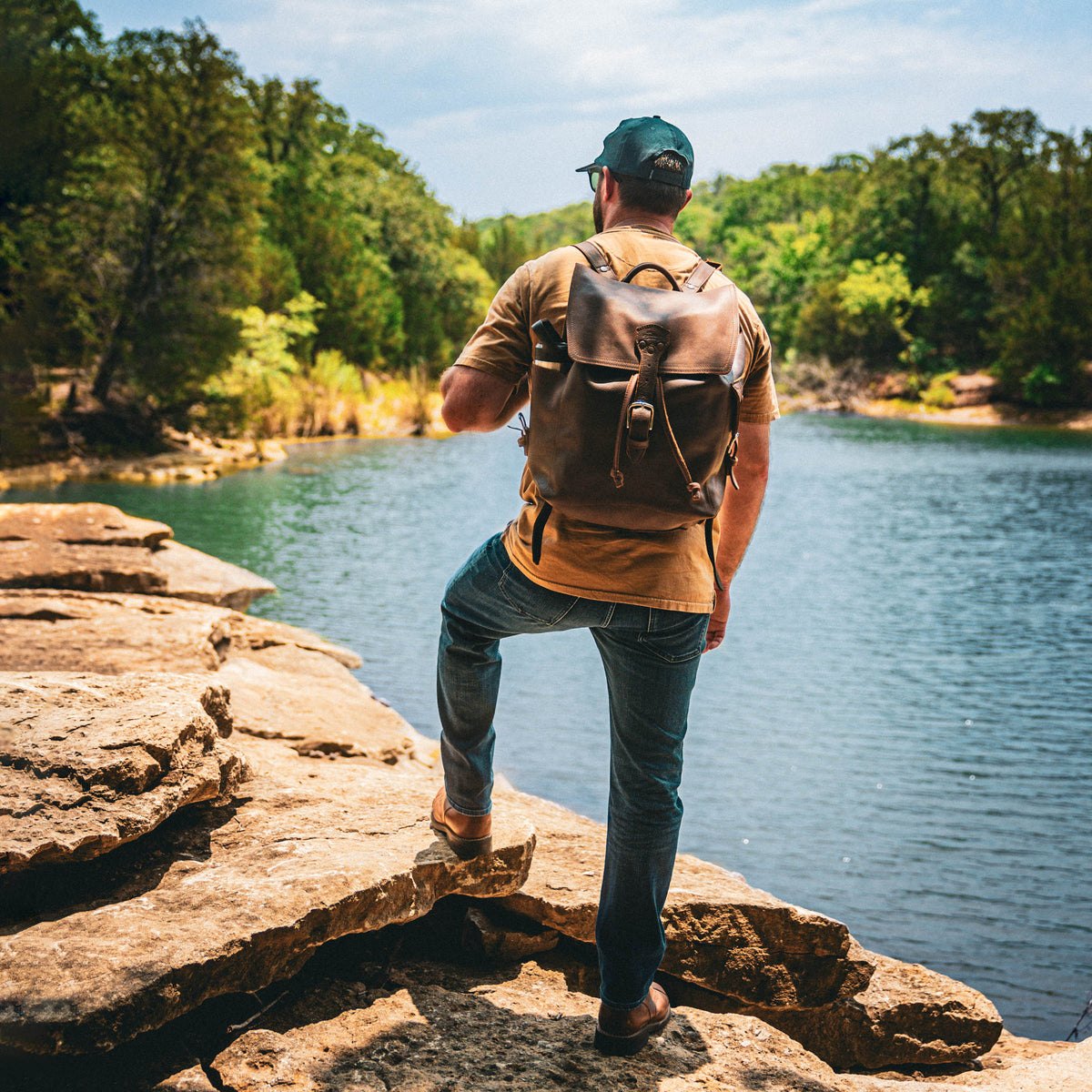 16" Drawstring Backpack in Dark Coffee Brown, worn by a man standing on rocks by a lake