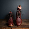 Officer Boot in Oxblood, staggered pair with dark laces and boot trees on a wooden table