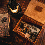 Leather Desk Box in Tobacco, open and holding old photographs beside a lit lantern and stacked books