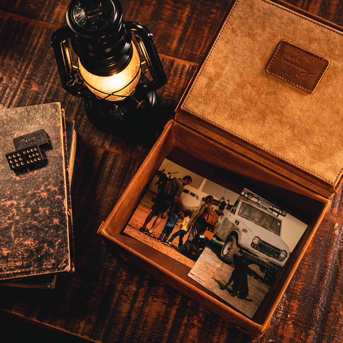 Leather Desk Box in Tobacco, open and holding old photographs beside a lit lantern and stacked books