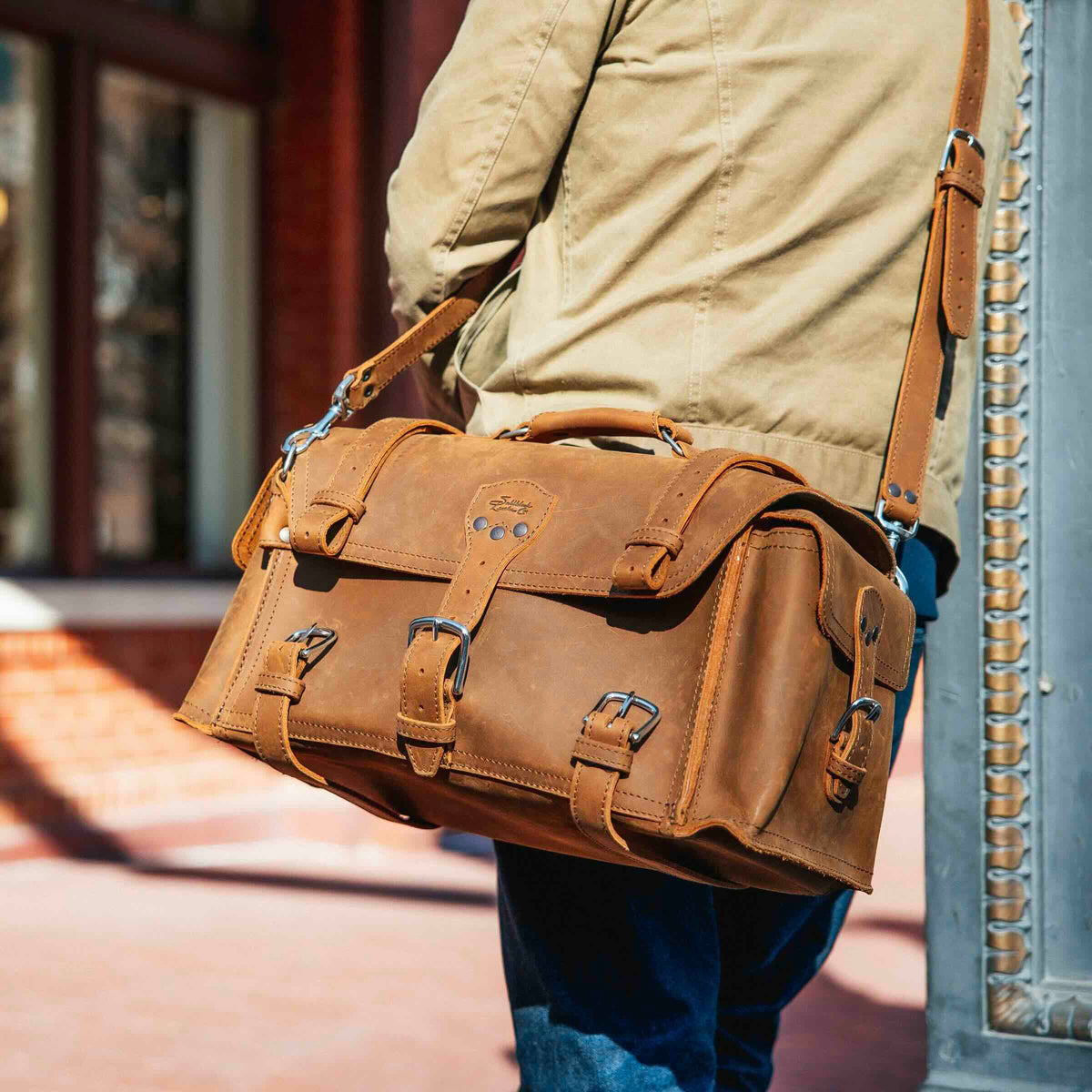 Side Pocket Leather Duffle in Tobacco carried on the shoulder strap by a man walking down a city street