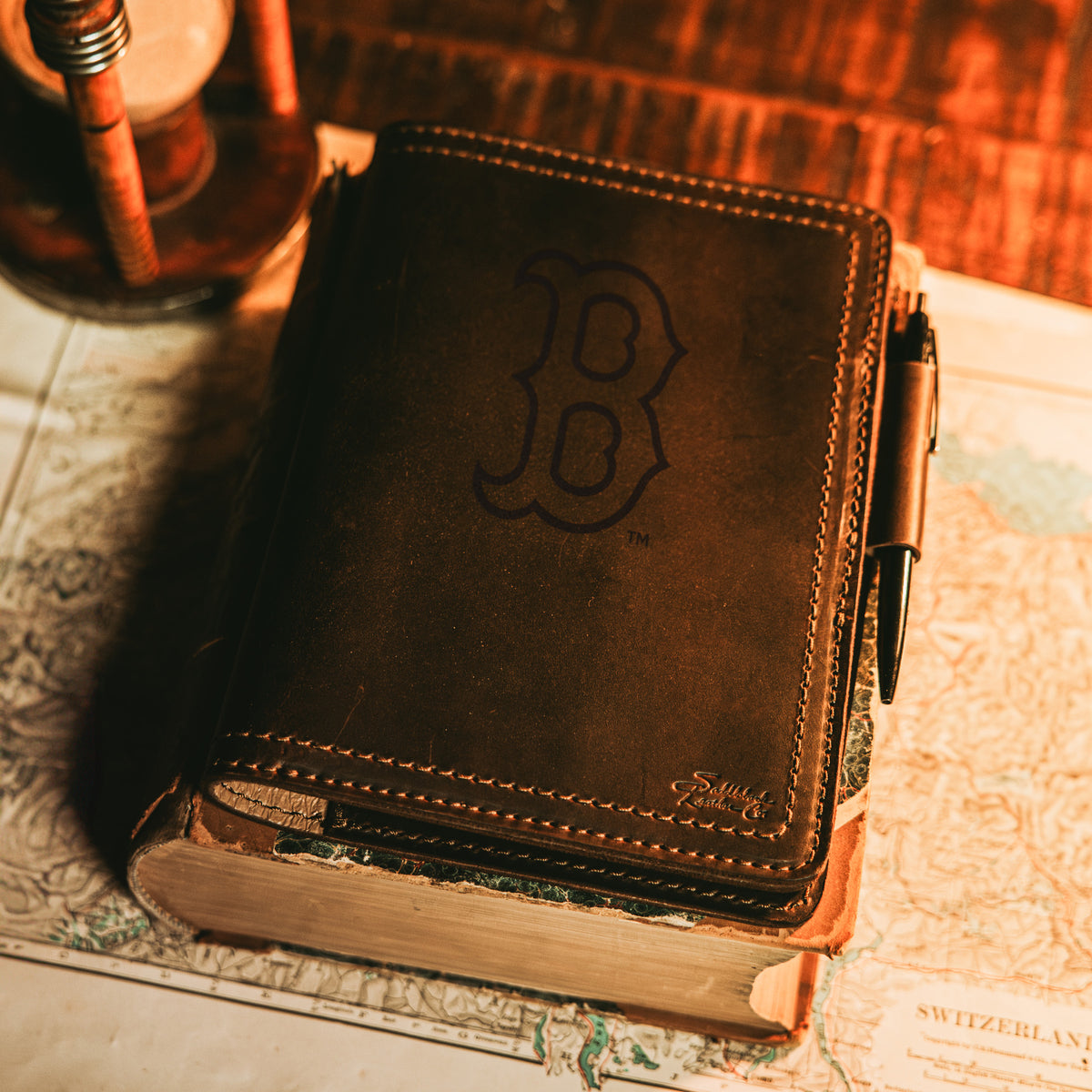 Leather Journal Cover - Boston Red Sox in Dark Coffee Brown with a pen, resting on an old book over a vintage map