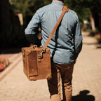 Grandfather Overnight Case in Tobacco carried by its shoulder strap by a man walking down a brick path