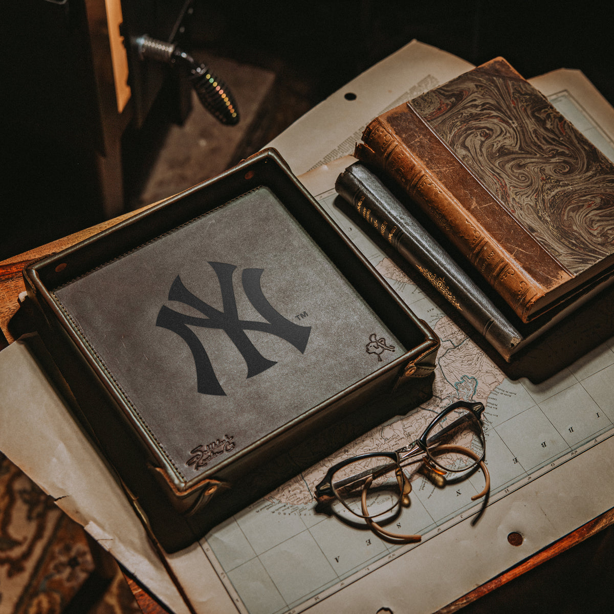 New York Yankees Leather Valet Tray in Dark Coffee Brown on a map beside old books and wire-rim glasses