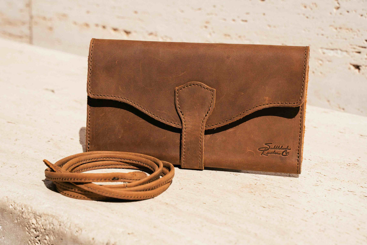 On The Go Leather Wallet in Tobacco on a sunlit stone ledge with its coiled leather strap beside it