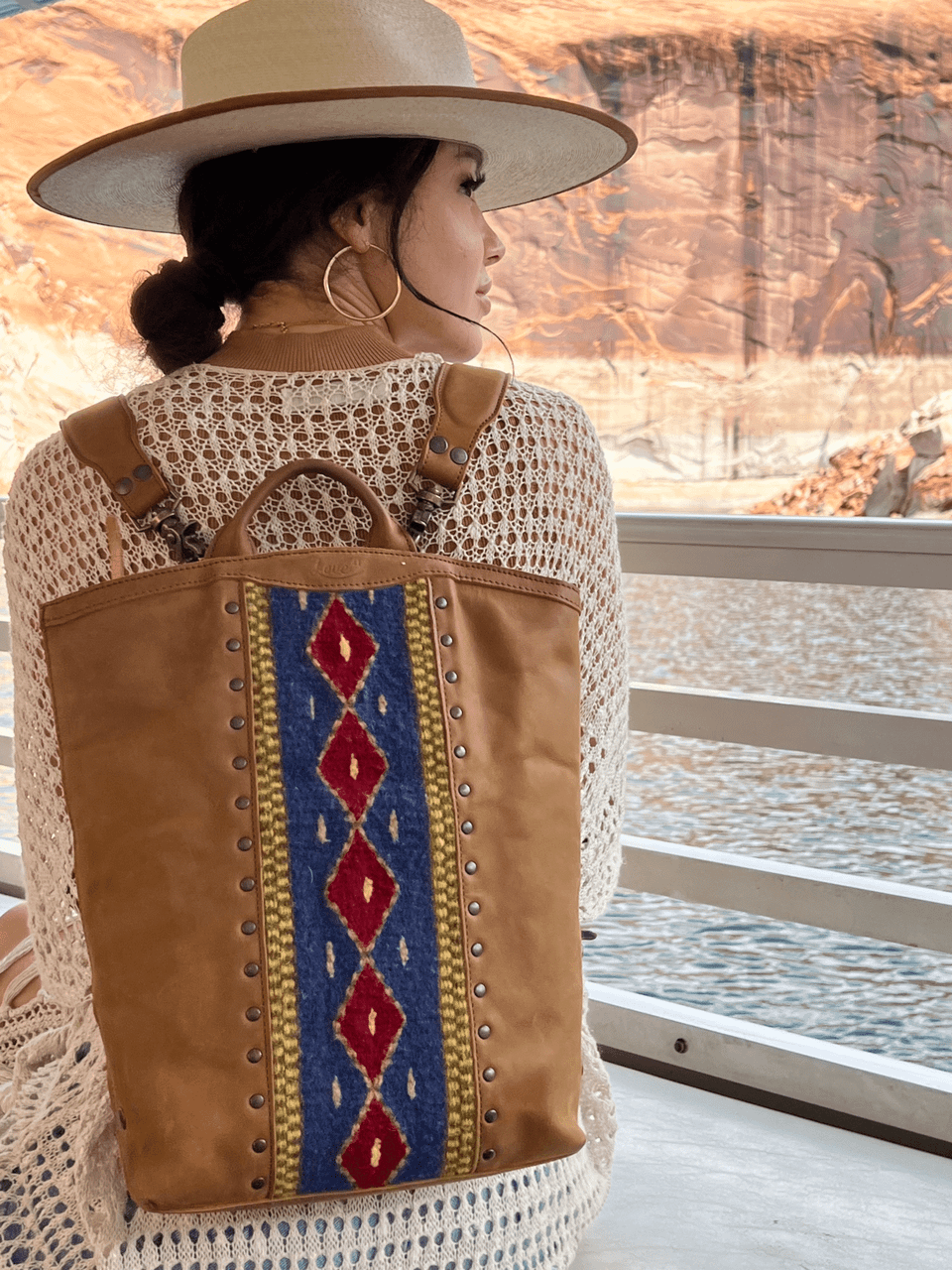 Lanita Leather Backpack in tan, worn by a woman in a wide-brim hat on a boat by canyon walls