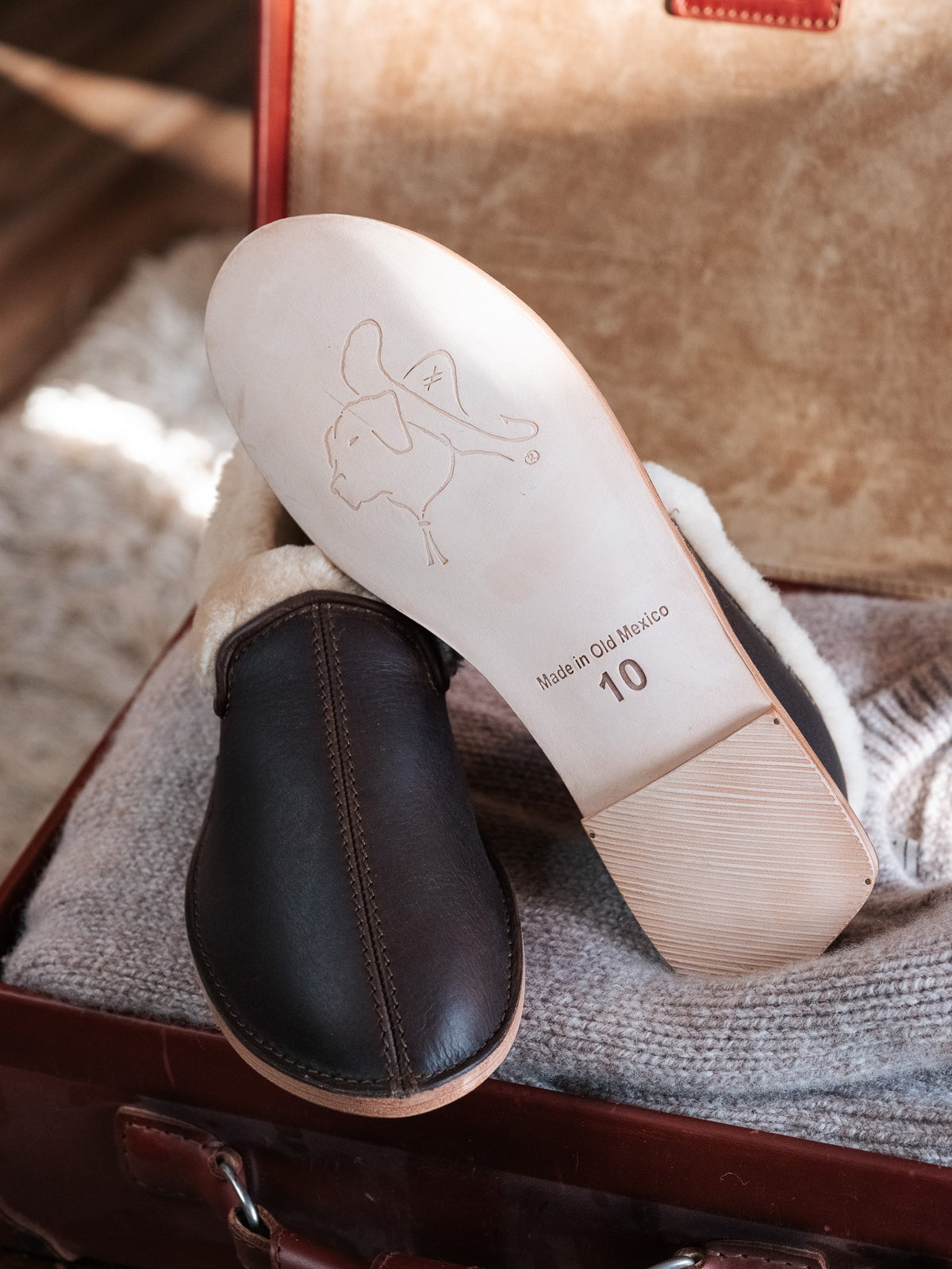Sheepskin Moccasins - New Design in Dark Coffee Brown, leather outsole with embossed logo, resting in an open suitcase