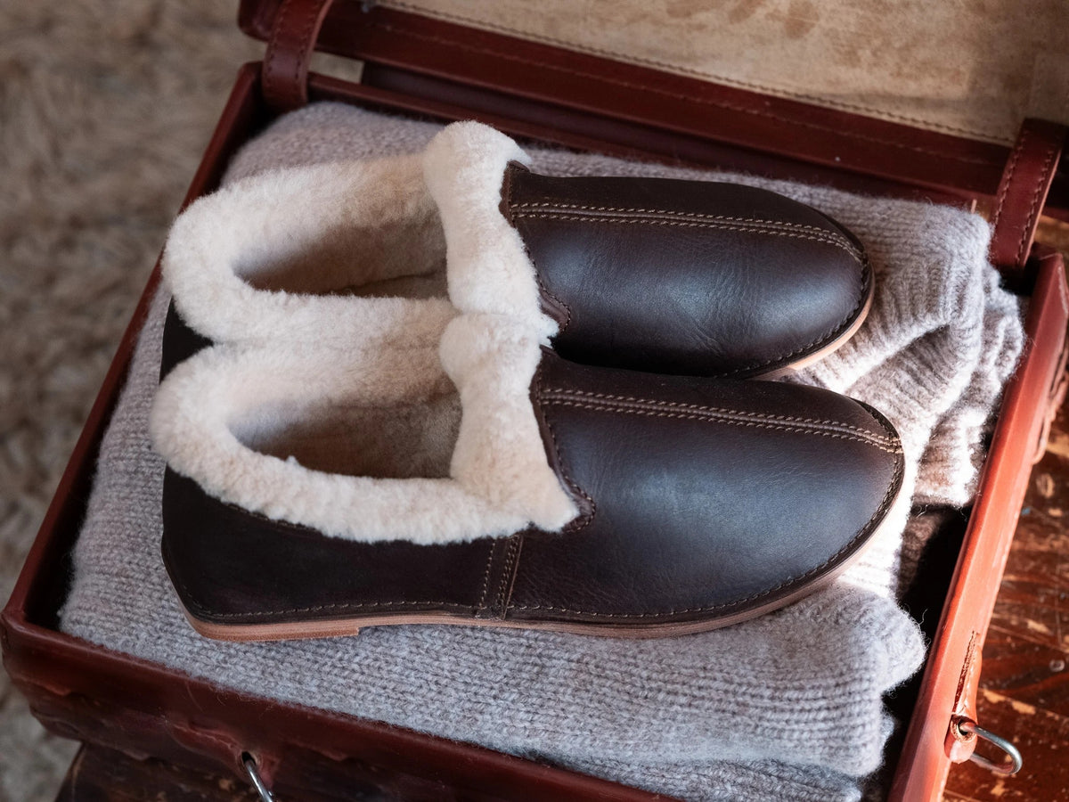 Sheepskin Moccasins - New Design in Dark Coffee Brown, angled view of a pair on a sweater in a leather suitcase