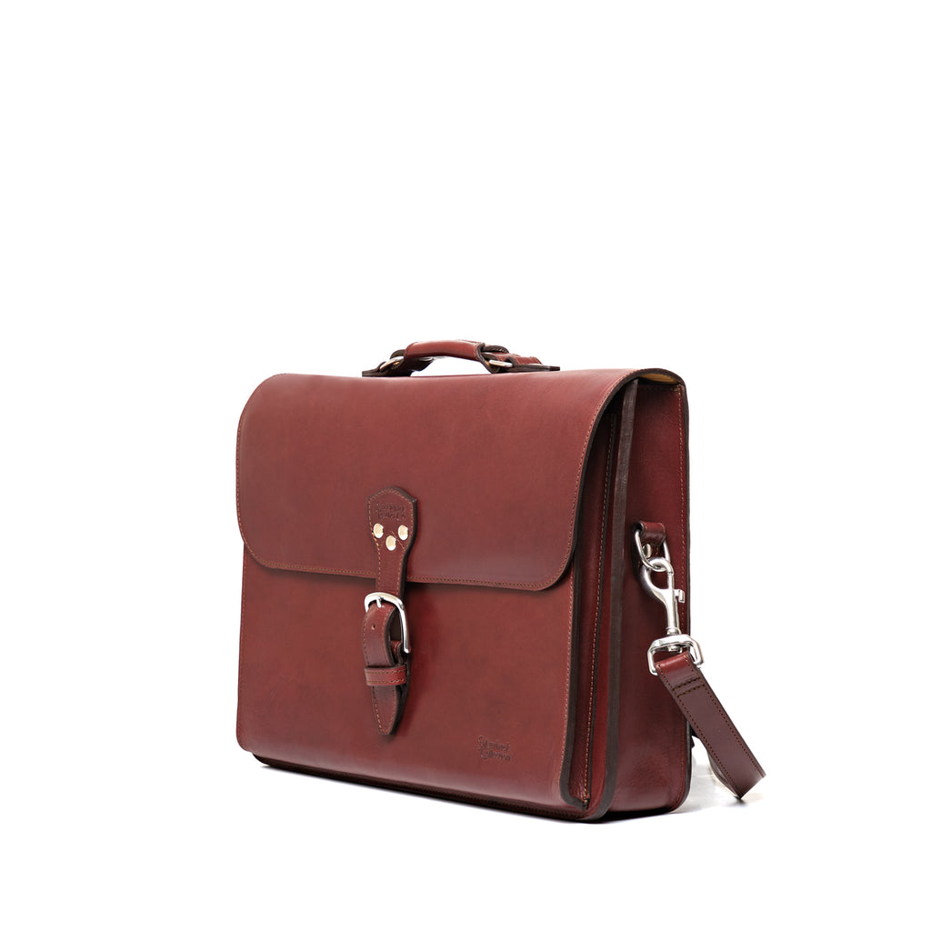 Livingstone Briefcase in Oxblood, angled side view showing the buckled flap and shoulder strap clip