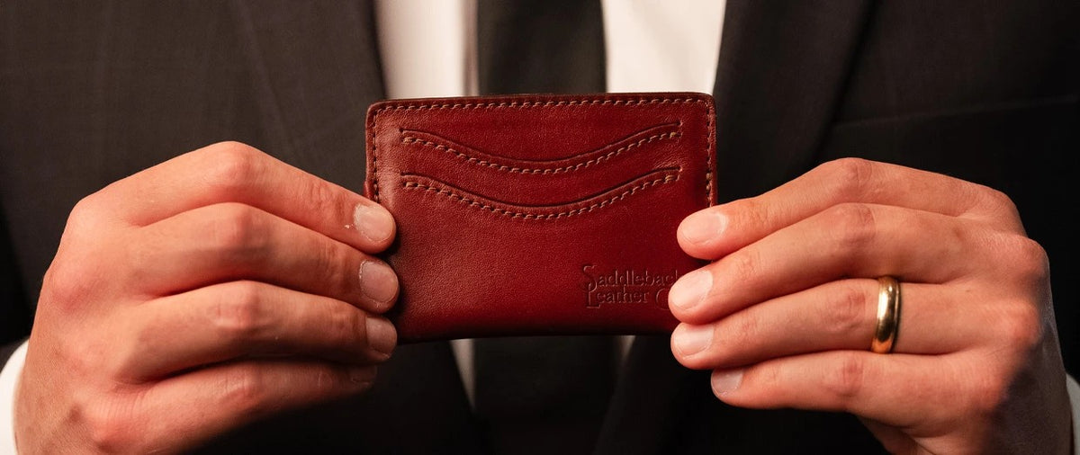 Newton Wallet in Oxblood, close-up of the slim card wallet held in both hands in front of a dark suit