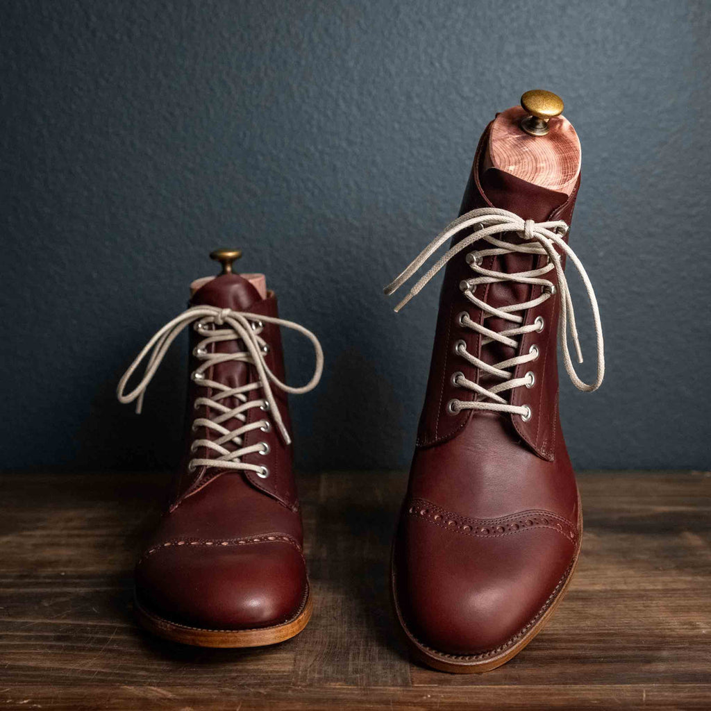 Officer Boot in Oxblood, pair with cream laces and boot trees on a wooden surface