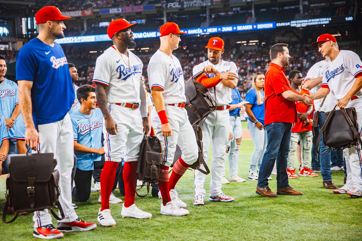 Texas Rangers All-Stars lined up on the field in front of a crowd, holding their new dark brown Tank Leather Backpacks.