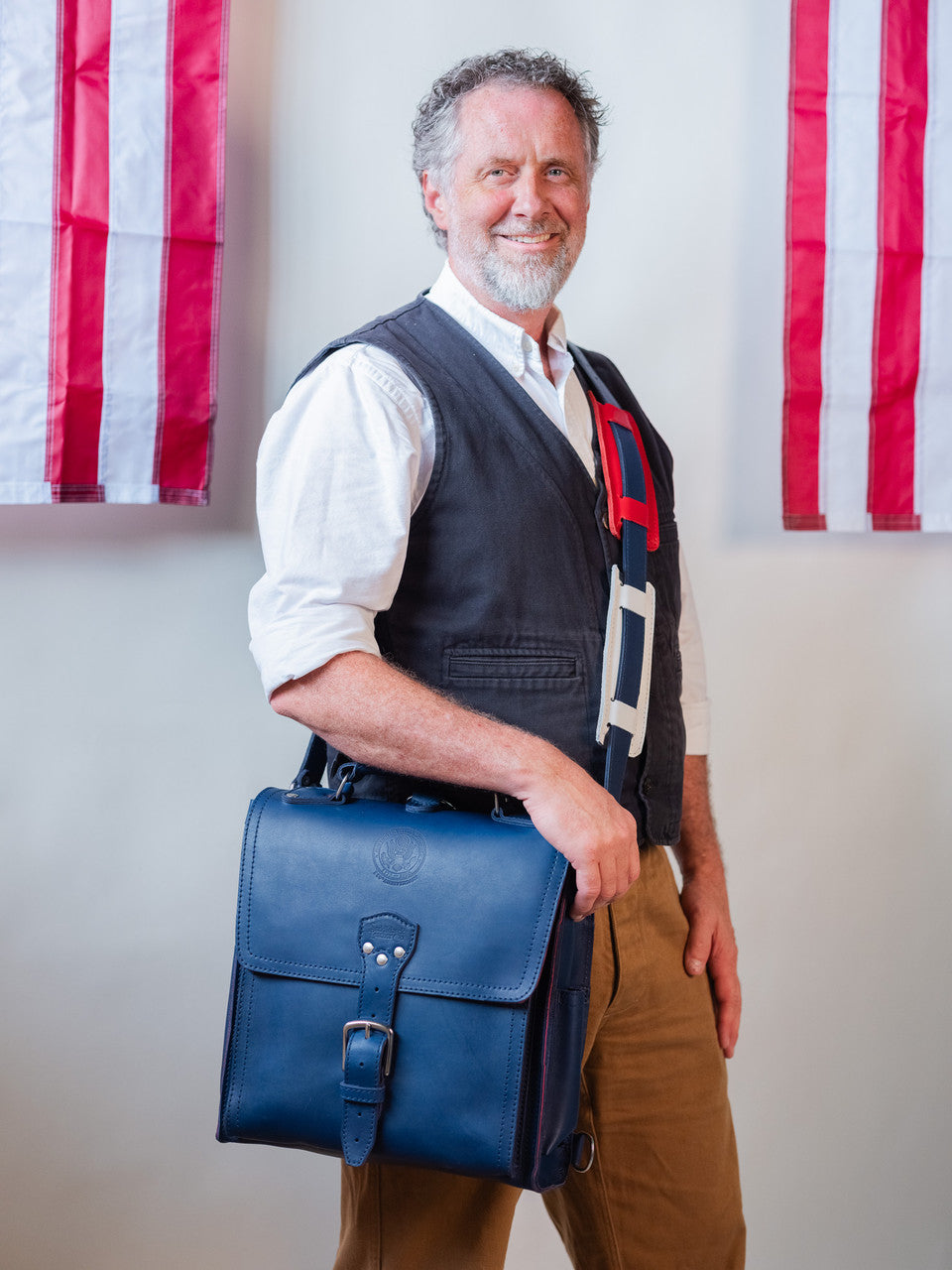 Saddleback Club Membership Paul Revere Leather Messenger Bag Backpack in Red, White and Blue, carried crossbody by a smiling man