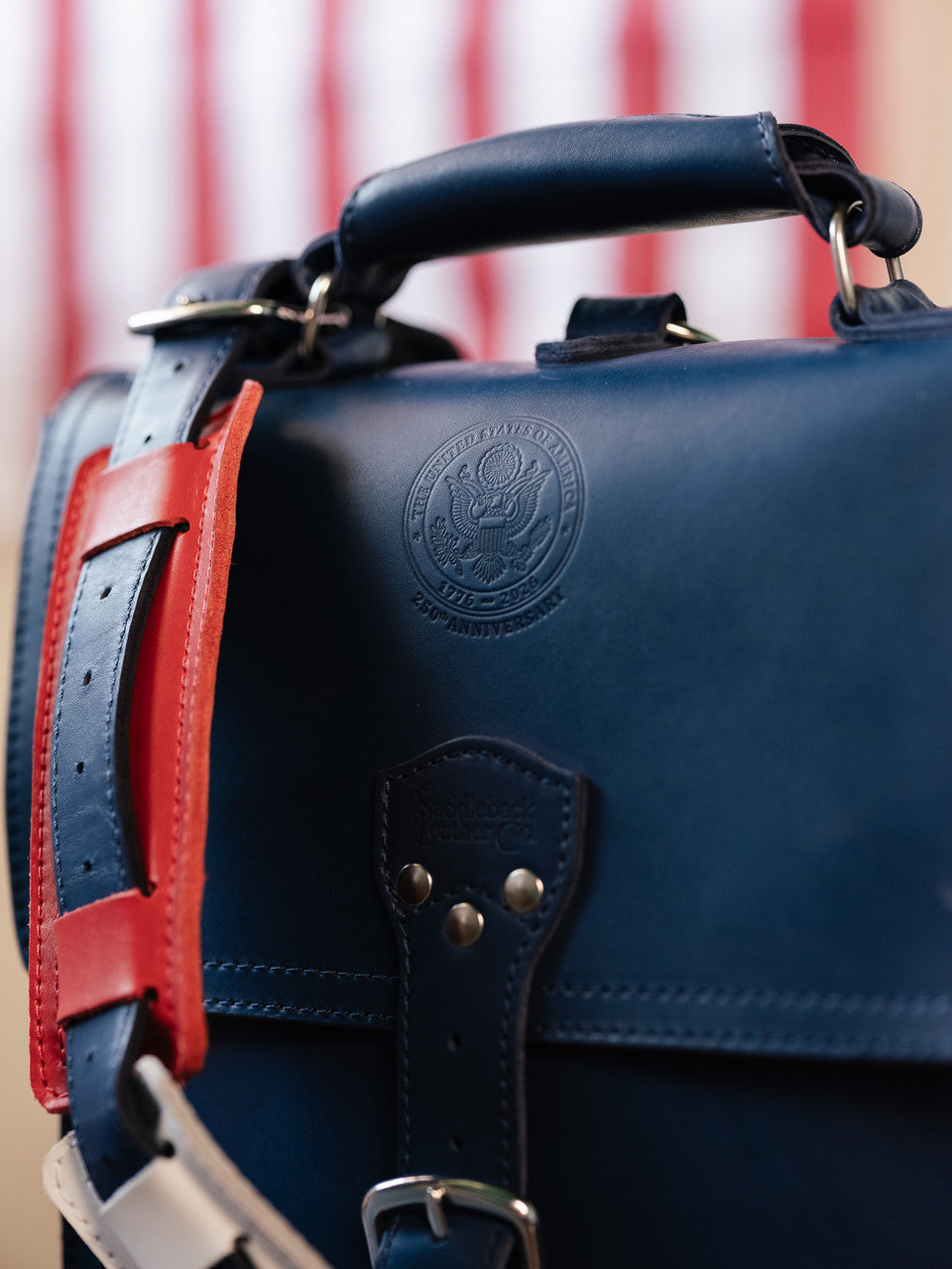 Saddleback Club Membership Paul Revere Leather Messenger Bag Backpack in Red, White and Blue, close-up of embossed seal and handle