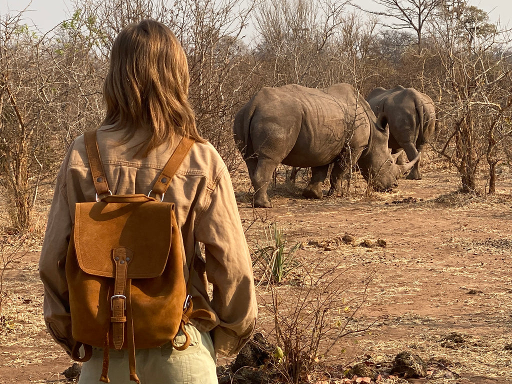 12" Drawstring Backpack in Tobacco, worn by a woman watching two rhinos in the African bush