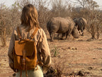 12" Drawstring Backpack in Tobacco, worn by a woman watching two rhinos in the African bush