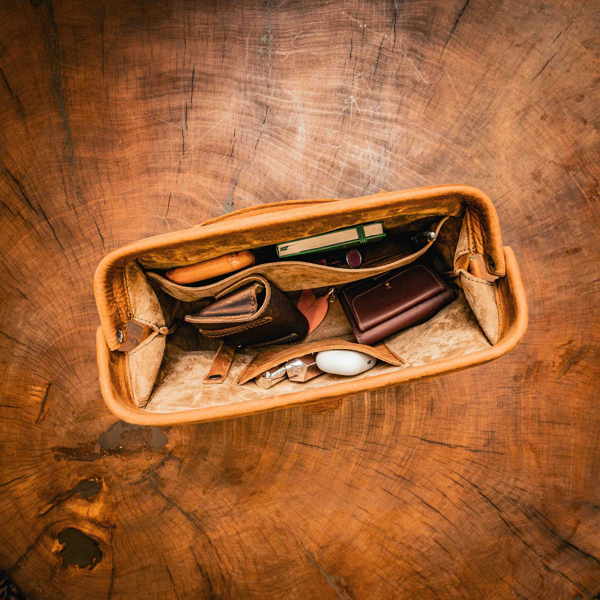 Everyday Purse in Tobacco, top view open on a wood stump showing a wallet, small leather cases and essentials in its pockets