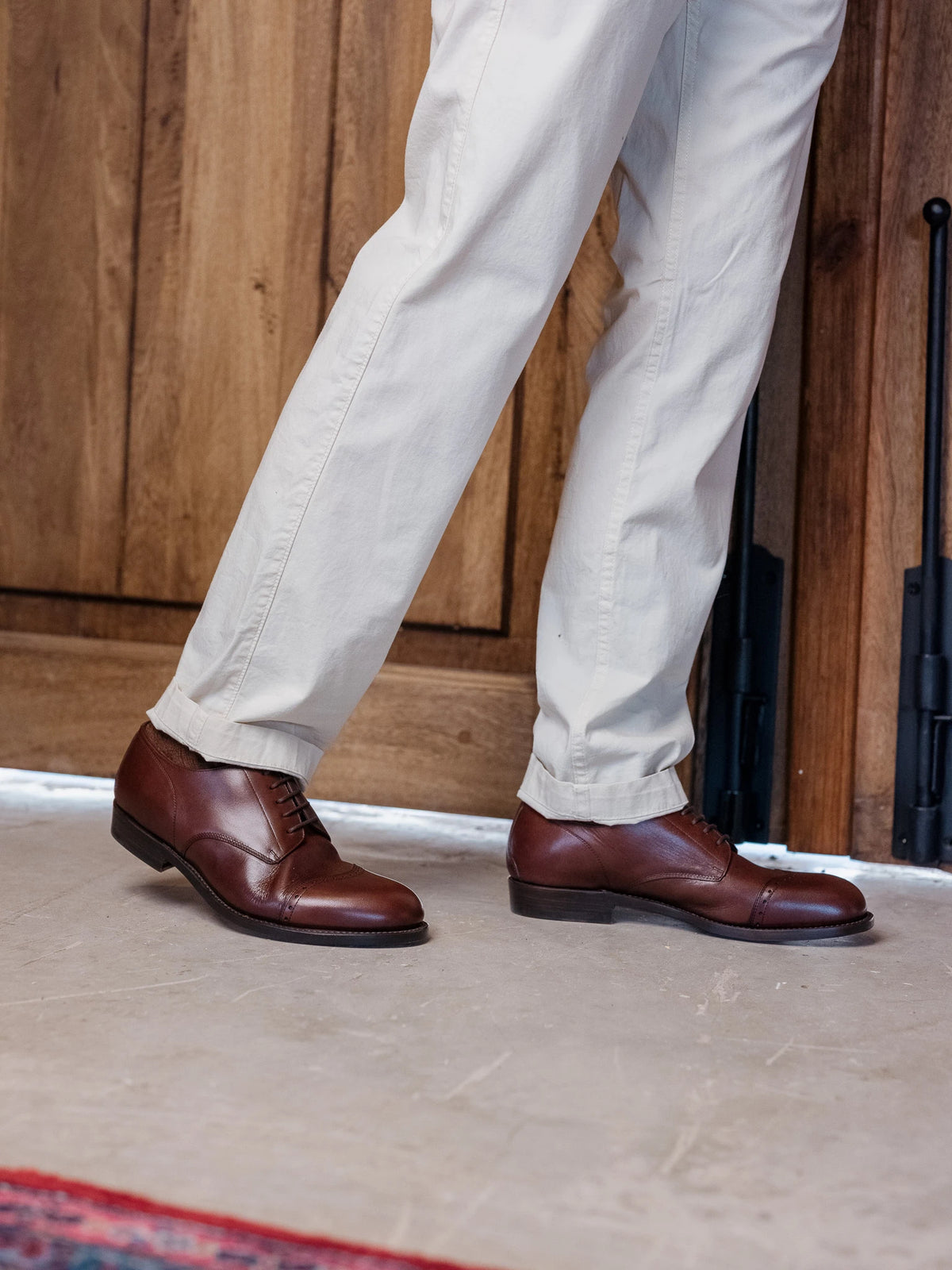 Toe Cap Shoes - Dark Oak on foot, a person in cream trousers mid-stride before a wooden door