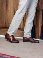 Toe Cap Shoes in Dark Oak, worn with light trousers on a concrete floor by a wooden door