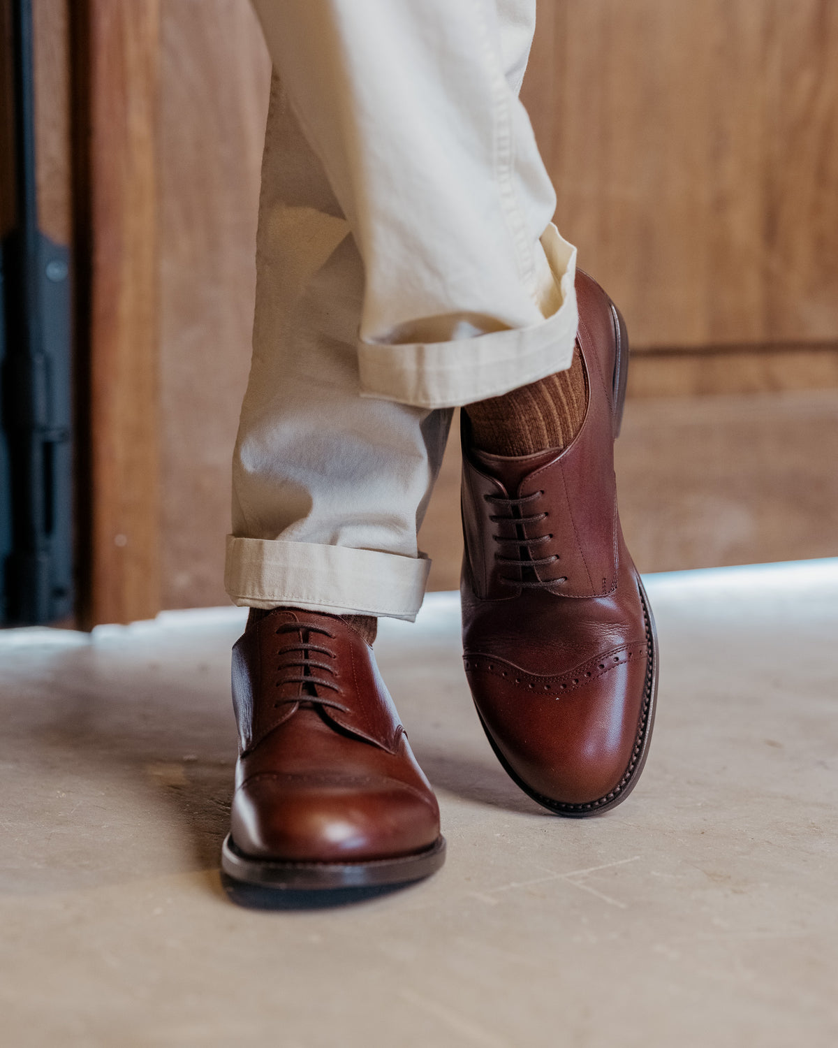 Toe Cap Shoes in Dark Oak, worn mid-stride with cuffed cream trousers