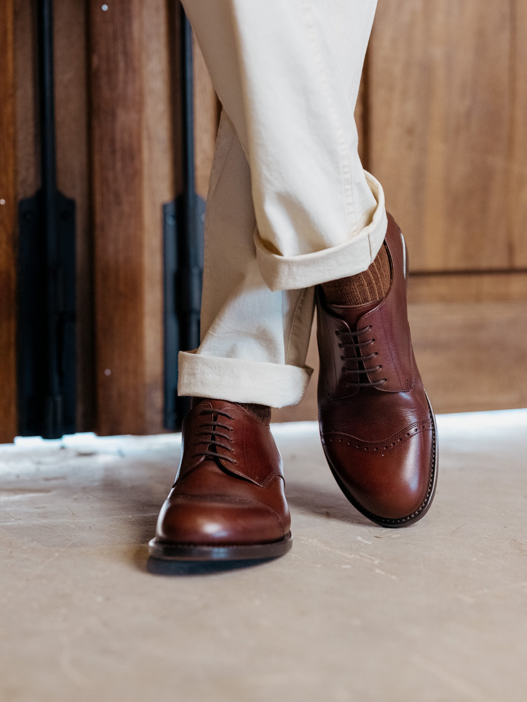 Toe Cap Shoes in Dark Oak, worn with legs crossed in front of a wooden door