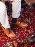 Toe Cap Shoes in English Tan, worn with cuffed cream trousers and dark socks on a red rug