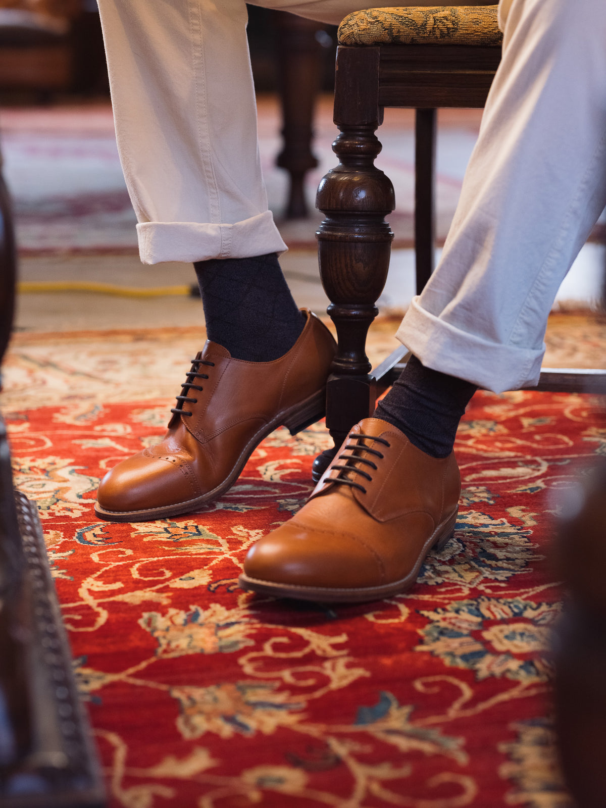 Toe Cap Shoes in English Tan, worn with dark socks beside a wooden chair on a red rug