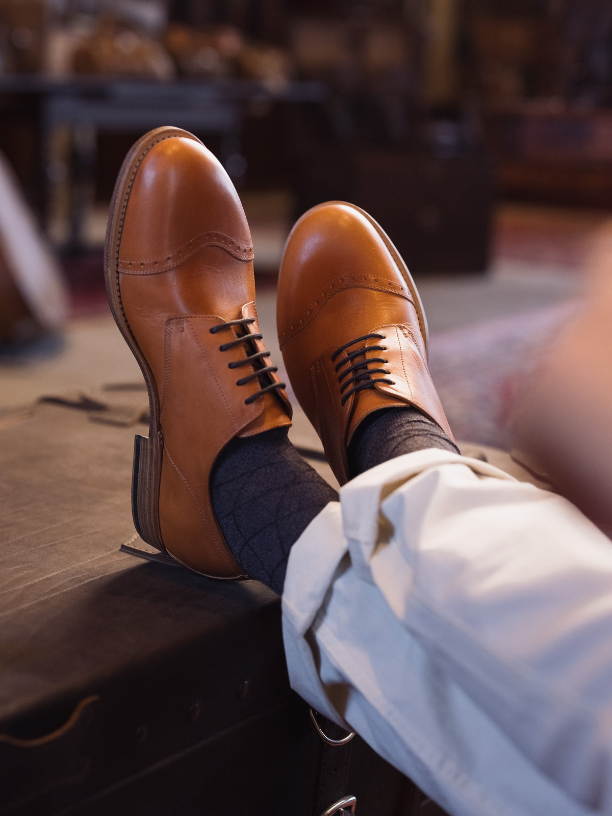 Toe Cap Shoes in English Tan, worn with crossed feet propped up on a dark trunk