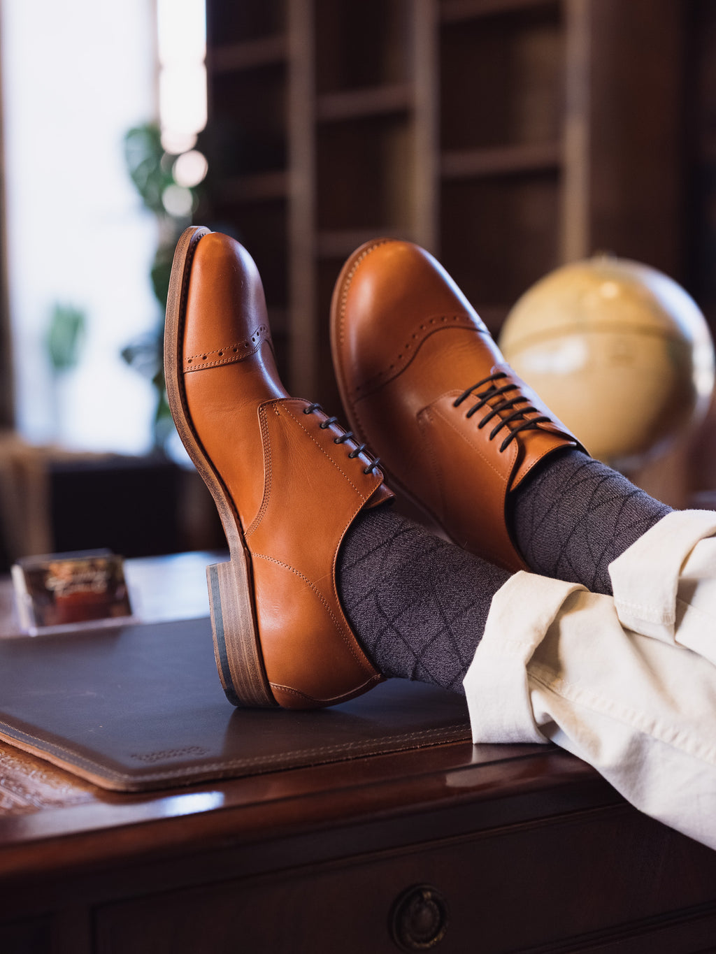 Toe Cap Shoes in English Tan, worn with gray socks, feet propped on a wooden desk