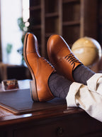 Toe Cap Shoes in English Tan, worn with gray socks, feet propped on a wooden desk