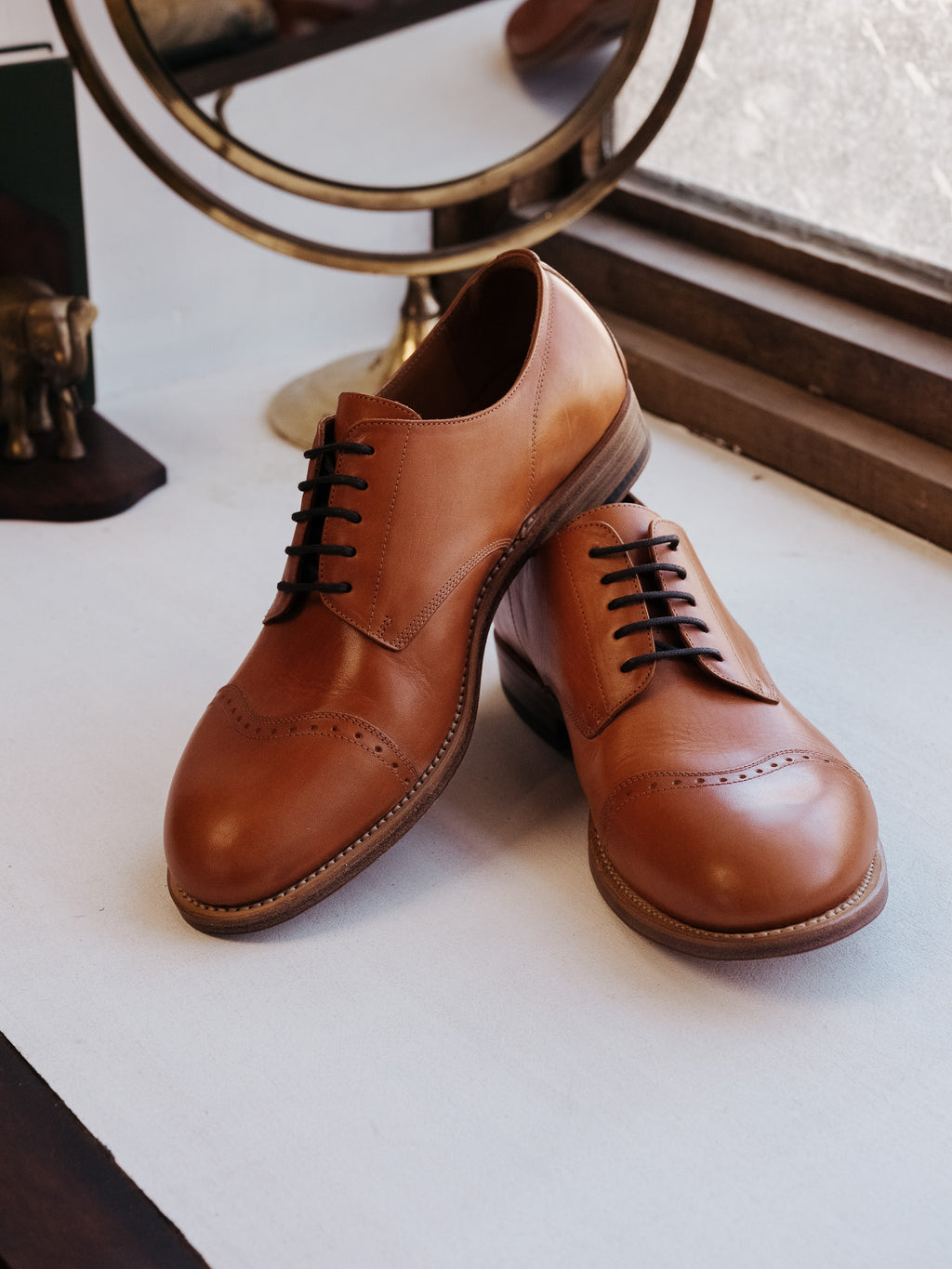 Toe Cap Shoes in English Tan, pair angled together by a window with a brass mirror