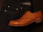 Toe Cap Shoes in English Tan, side view of one shoe resting on folded dark denim jeans