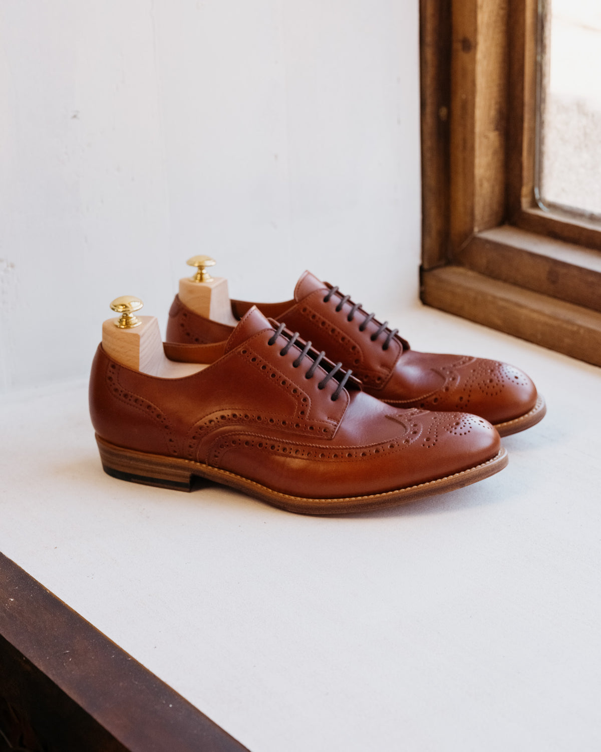 Wingtip Shoes in Chestnut, side view of pair with shoe trees on a windowsill