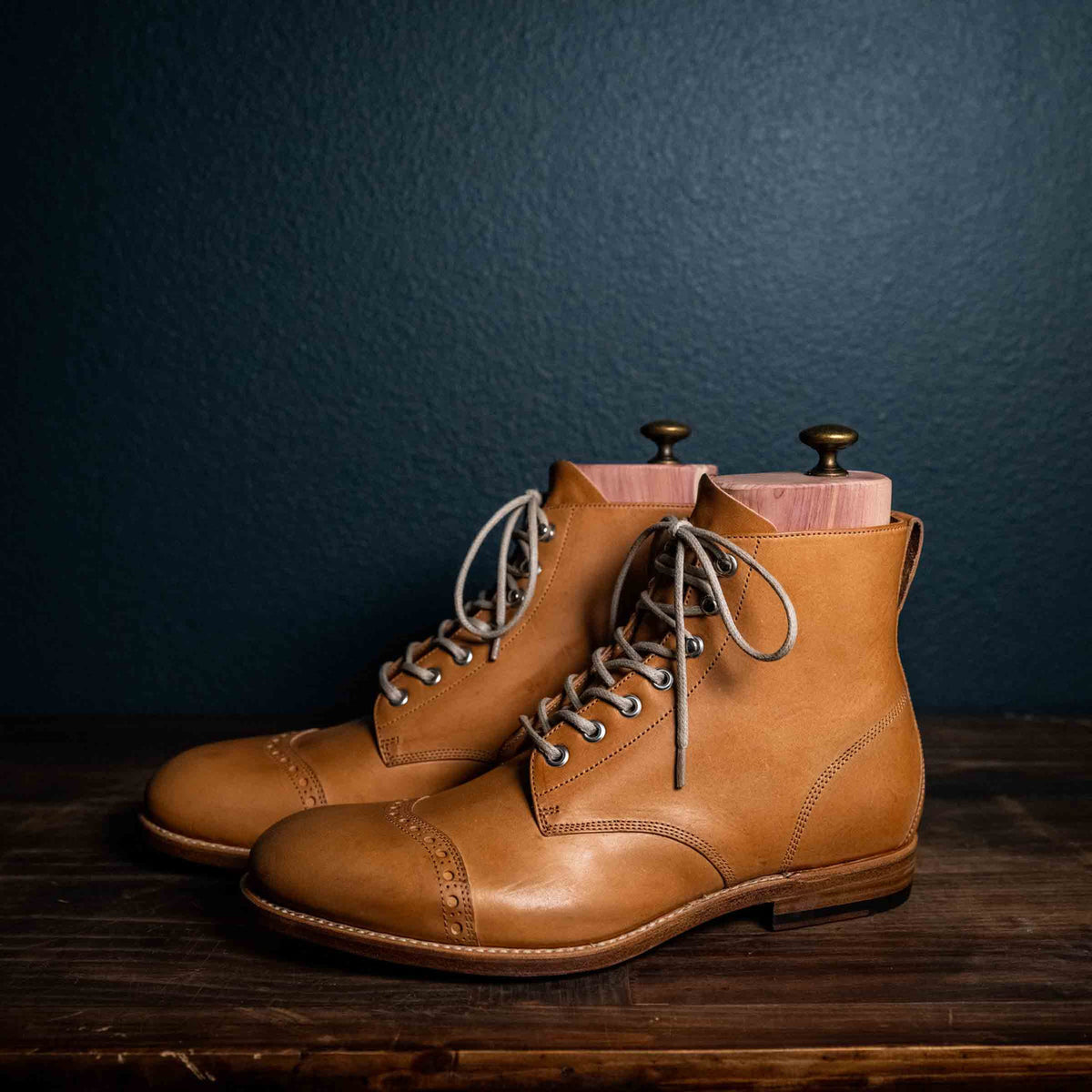 Pair of high quality English tan leather Officer's Boots with cedar shoe trees on a wooden table, angled front view