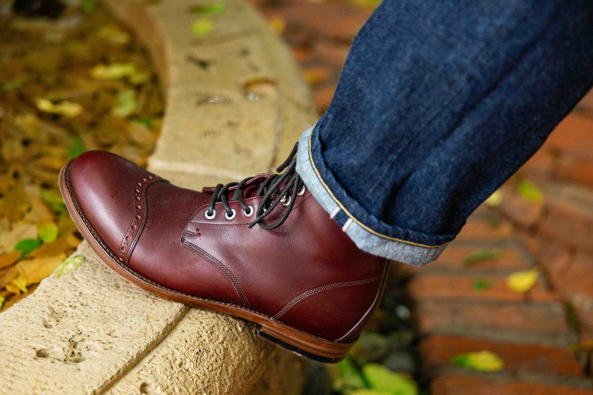 Officer's Boot in Oxblood, worn with cuffed jeans, foot resting on a stone step