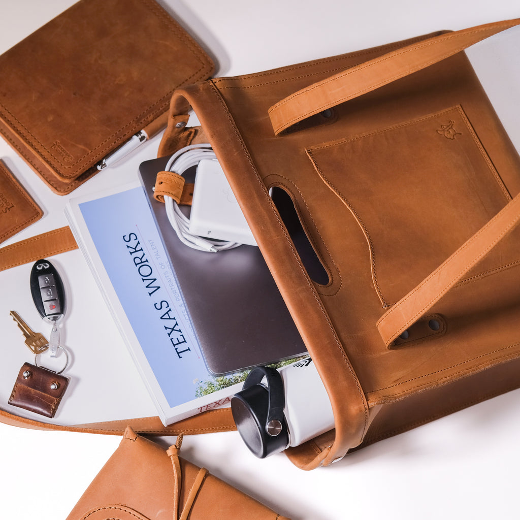 Professional Leather Tote in Tobacco on its side with a book, laptop, keys and leather accessories spilling out