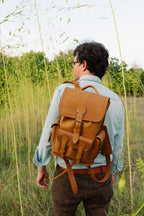Small Front Pocket Backpack in Tobacco worn by a man in glasses looking over his shoulder among tall grass