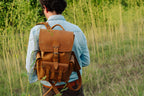 Small Front Pocket Backpack in Tobacco, close rear view on a man in a denim shirt walking through tall grass