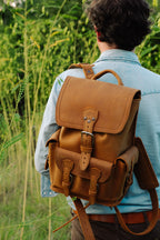 Small Front Pocket Backpack in Tobacco worn by a man in a denim shirt, seen from behind in tall grass