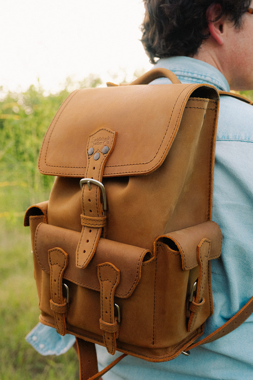 Small Front Pocket Backpack in Tobacco, close-up from behind on a man's back showing the flap, buckles and side pocket