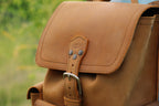 Small Front Pocket Backpack in Tobacco, close-up of the flap, embossed strap tab and steel buckle outdoors