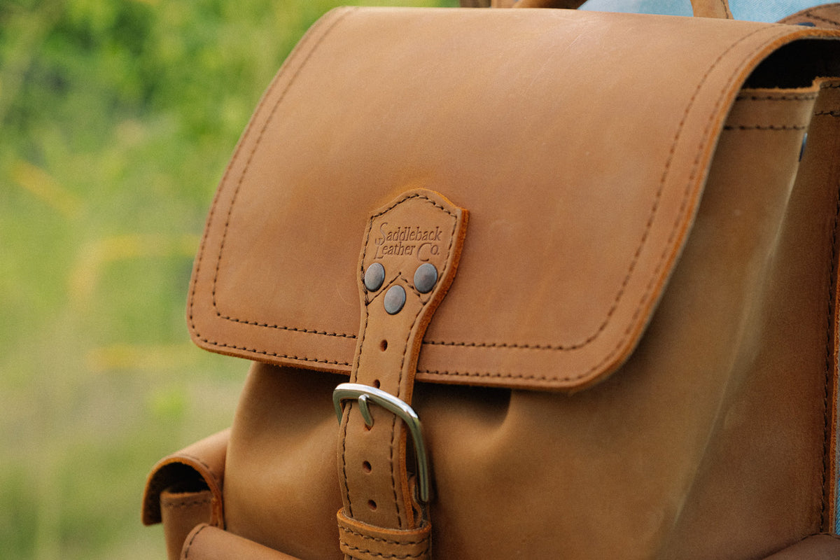 Small Front Pocket Backpack in Tobacco, close-up of the flap, embossed strap tab and steel buckle outdoors