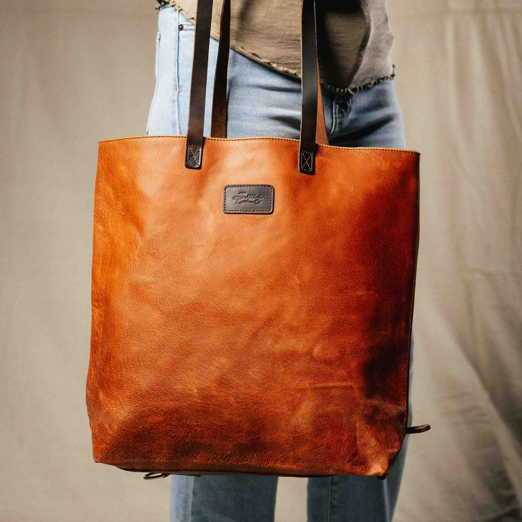 Travel Tote in Bacon carried on the shoulder by a person in jeans, front view with leather logo patch