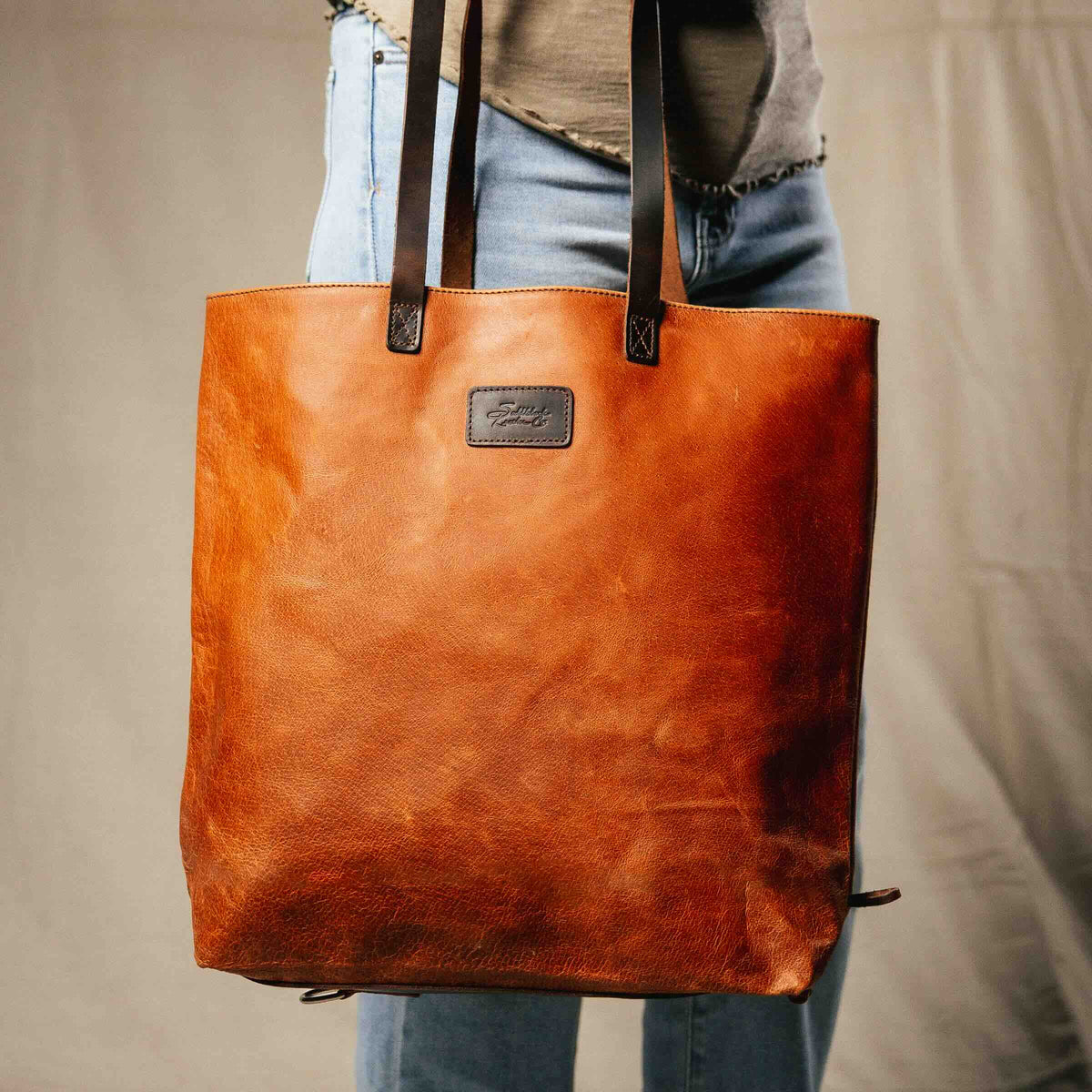 Travel Tote in Bacon carried on the shoulder by a person in jeans, front view with leather logo patch