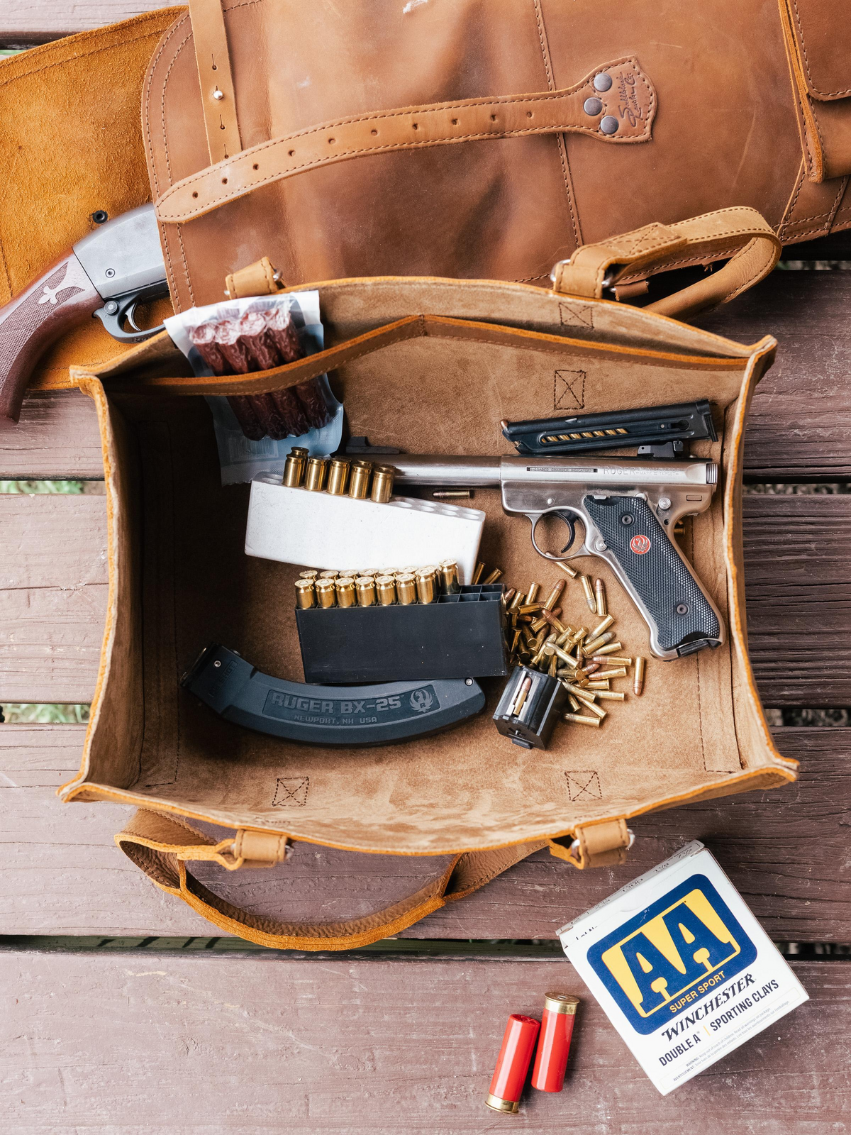 Open brown leather Tool Tote holding a pistol, magazine, and ammunition on a wooden deck